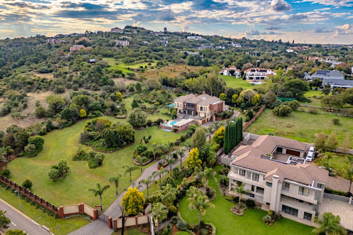 Aerial view of a large residential property featuring a swimming pool, extensive landscaped gardens, and a paved driveway within a suburban estate setting.