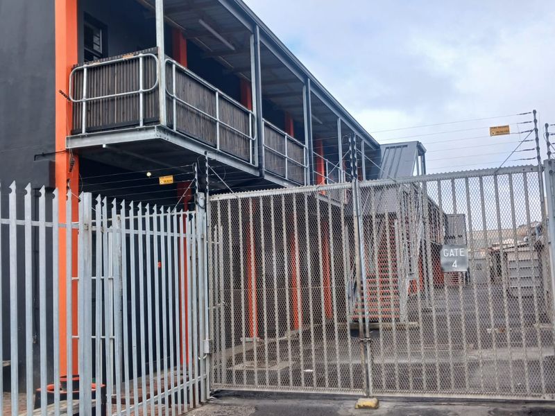 Industrial property exterior featuring secure perimeter fencing, electric security wires, and external access staircases leading to upper-level balcony walkways.