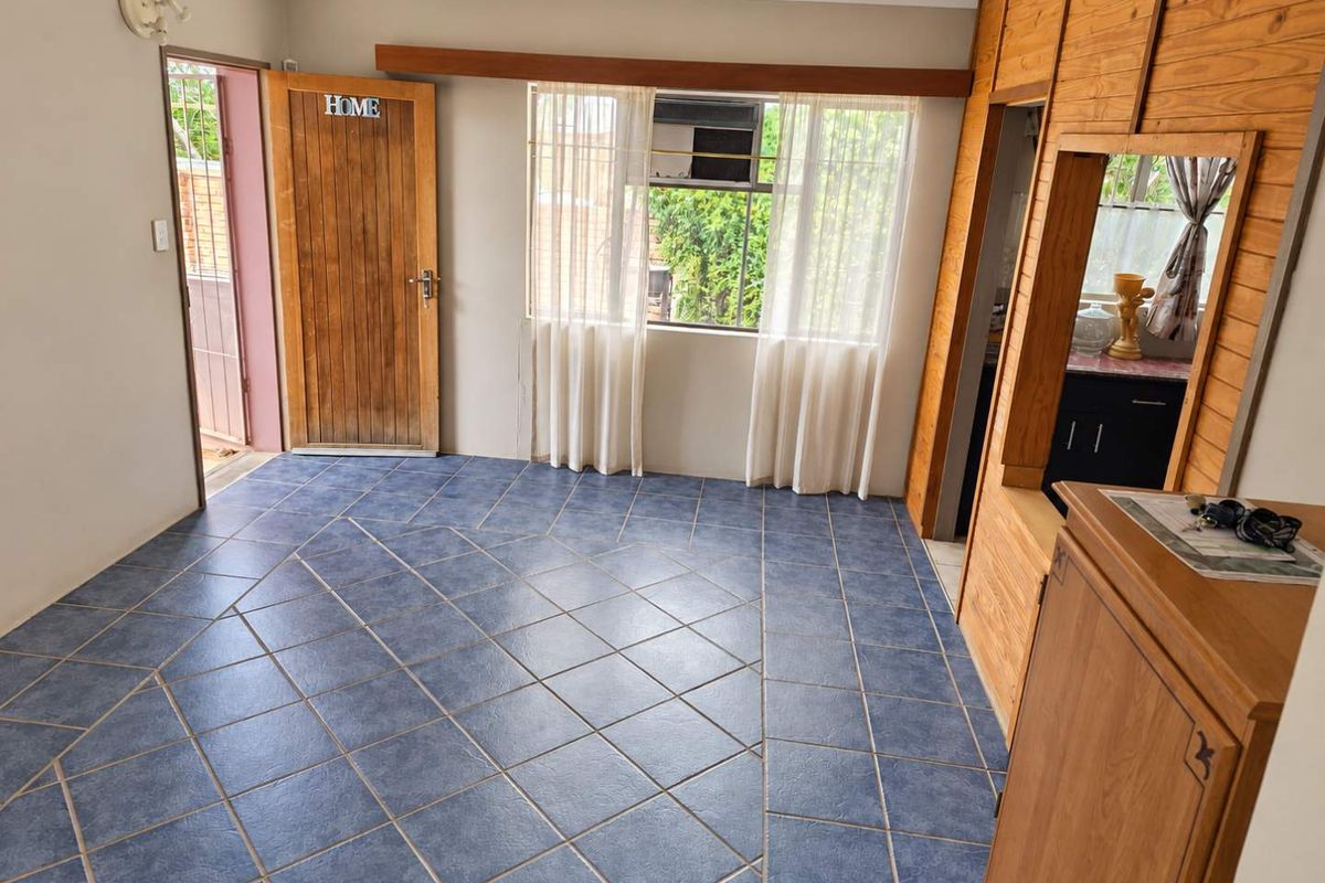 An empty living area featuring blue tiled flooring, timber wall paneling, and a window-mounted air conditioning unit.