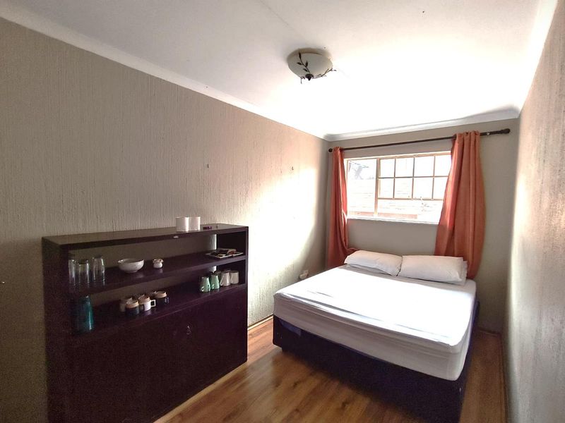 A functional bedroom featuring laminate flooring, textured wall finishes, and a window with grid panes, providing a simple and practical living space.