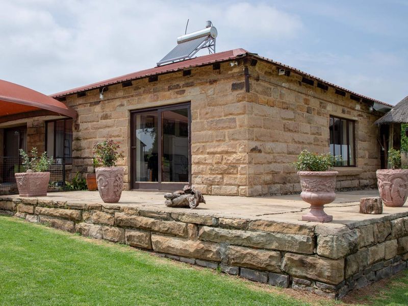 A charming farmhouse exterior featuring natural sandstone walls, a stone patio, and a roof-mounted solar water heating system.