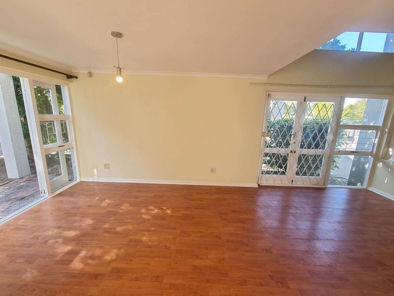 An empty living room featuring laminate flooring, a skylight, and access to the exterior through a sliding glass door with a security gate.
