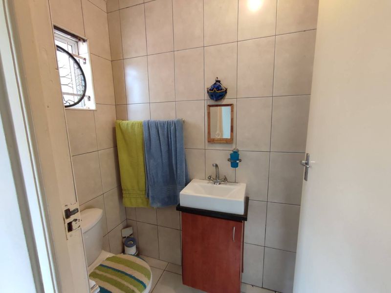 A compact guest bathroom featuring neutral wall tiles, a vanity cabinet with basin, and a standard toilet.