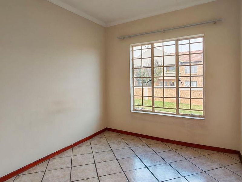 An empty bedroom featuring neutral wall paint, tiled flooring, and a large window fitted with security burglar bars.