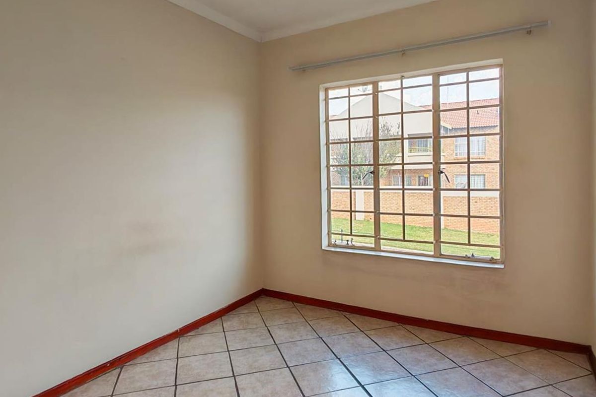 An empty bedroom featuring neutral wall paint, tiled flooring, and a large window fitted with security burglar bars.