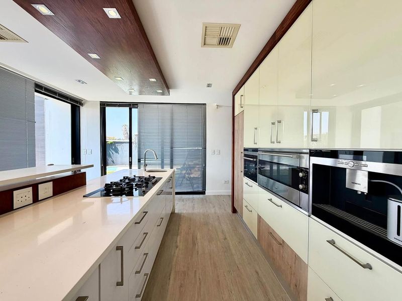 Modern kitchen featuring a large island with gas cooktop, high-gloss cabinetry, integrated Siemens appliances, and stone countertops with direct access to the patio.