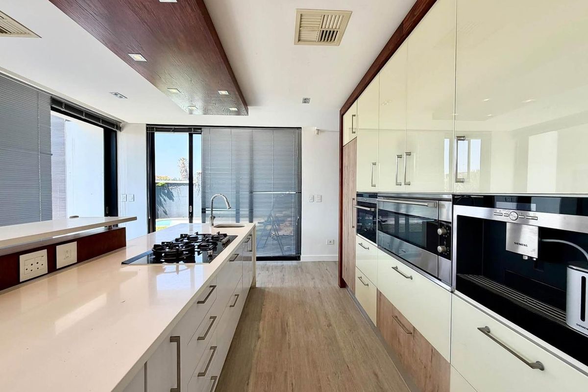 Modern kitchen featuring a large island with gas cooktop, high-gloss cabinetry, integrated Siemens appliances, and stone countertops with direct access to the patio.