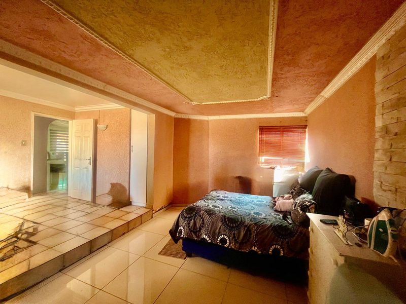 Spacious bedroom featuring a raised floor platform, textured ceiling with crown molding, and tiled flooring, offering potential for a modern renovation.