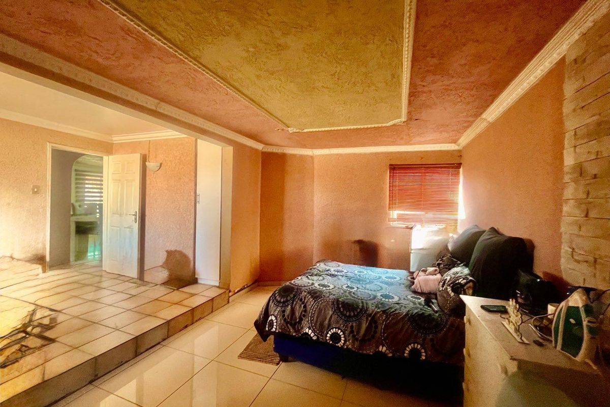 Spacious bedroom featuring a raised floor platform, textured ceiling with crown molding, and tiled flooring, offering potential for a modern renovation.