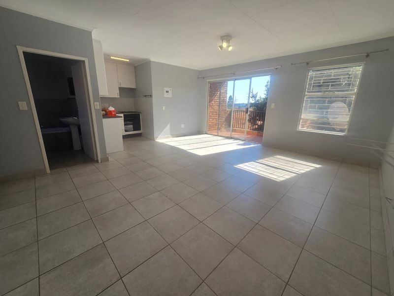 Spacious open-plan living area featuring tiled floors, a compact kitchen with built-in cabinetry, and direct access to a balcony through sliding glass doors.