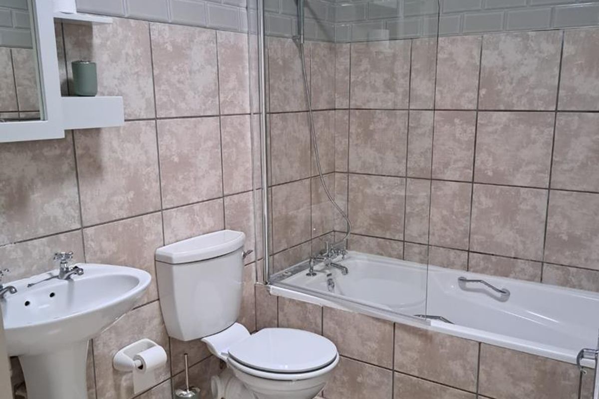 A functional bathroom featuring a pedestal basin, a toilet, and a bathtub with a glass shower screen and subway tile backsplash.