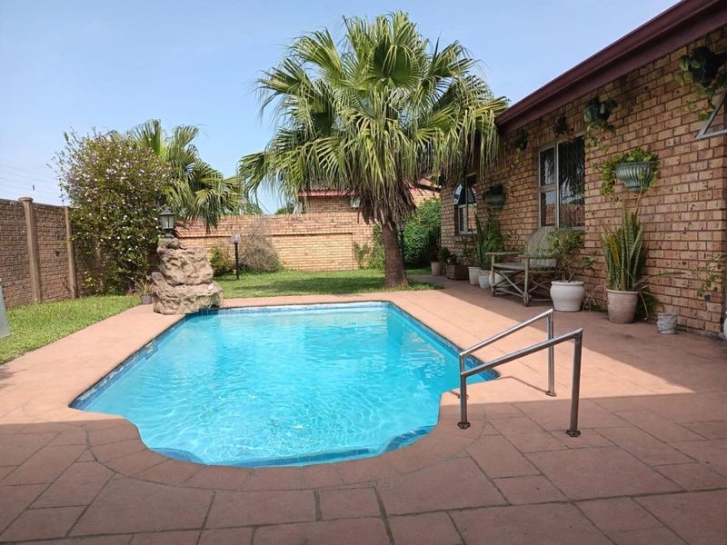 A private outdoor pool area featuring a paved deck, brick exterior wall, and established garden surroundings in a townhouse setting.