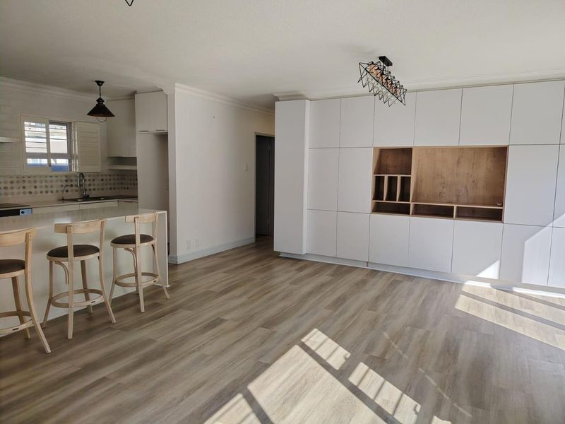 Modern open-plan living area featuring light wood-look laminate flooring, extensive built-in white cabinetry with integrated shelving, and a functional kitchen island.