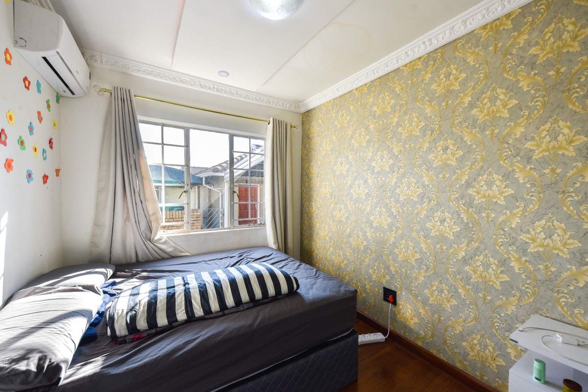 A bedroom featuring timber flooring, a decorative ceiling cornice, and a patterned wallpaper feature wall, equipped with a wall-mounted air conditioning unit.