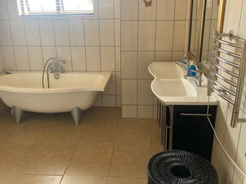 A functional bathroom featuring a freestanding bathtub, double vanity unit, and a wall-mounted heated towel rail with neutral floor and wall tiling.