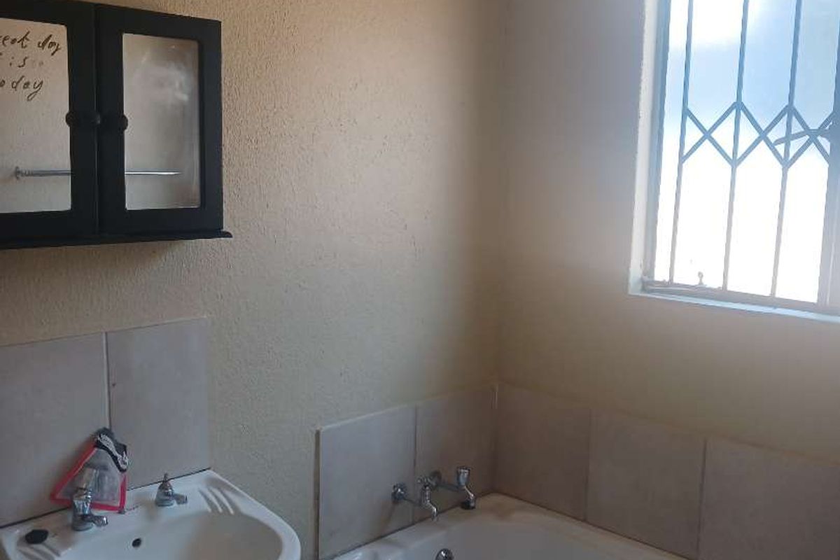 A functional bathroom featuring a built-in bathtub, wall-mounted basin, and tiled finishes, offering a clean and practical space.