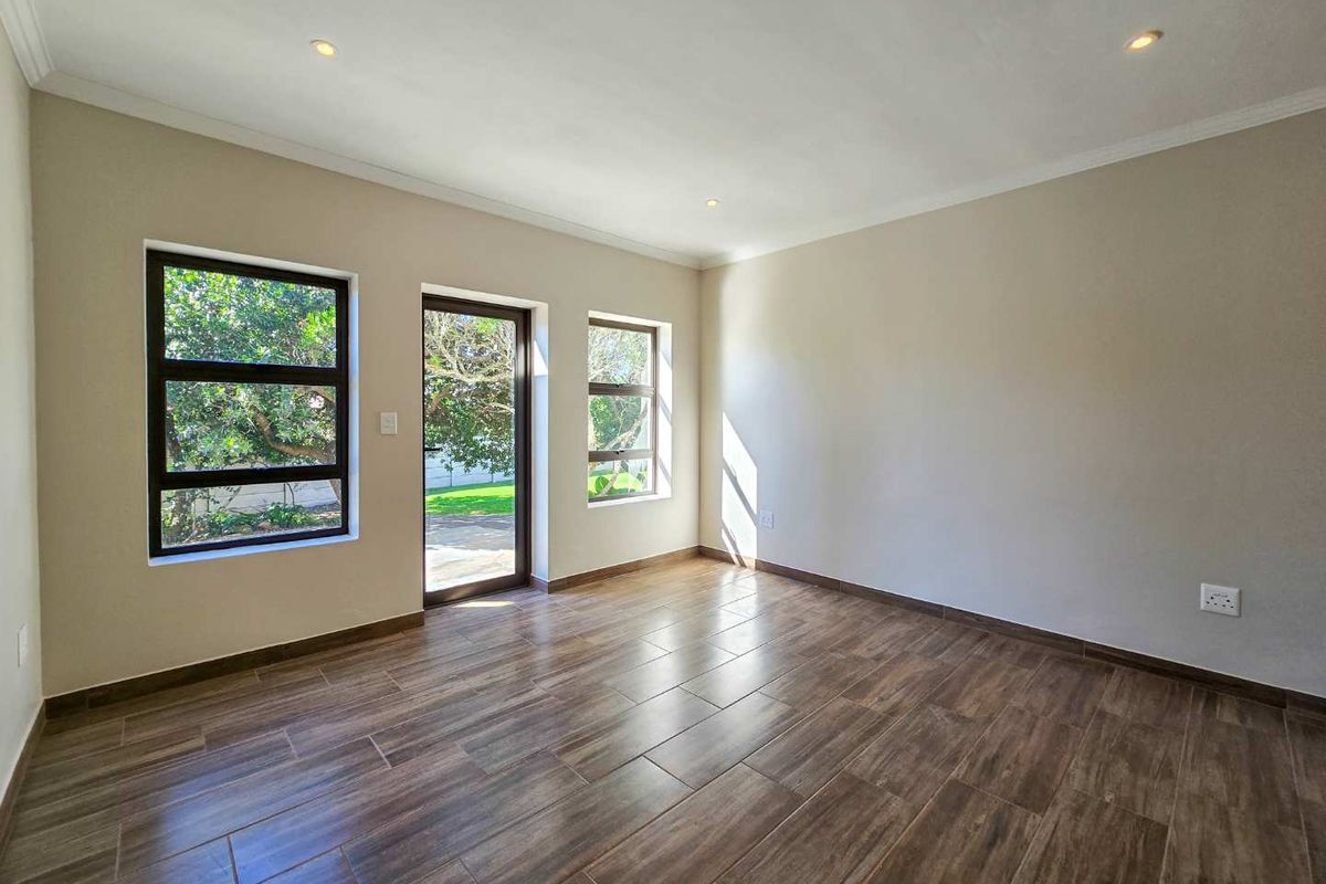 A bright, empty living room featuring modern wood-look tile flooring, recessed ceiling lighting, and large windows with direct access to the garden.