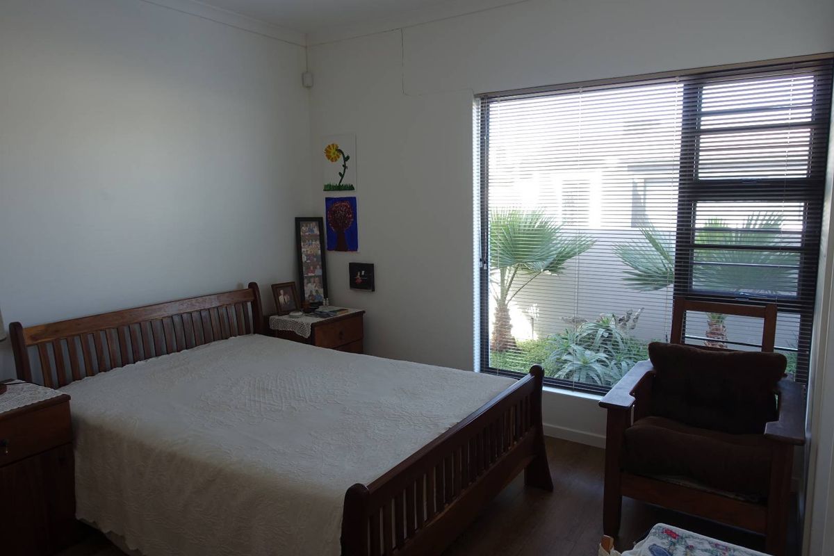 A bedroom featuring wood-look flooring, a large window with fitted blinds, and neutral wall finishes.