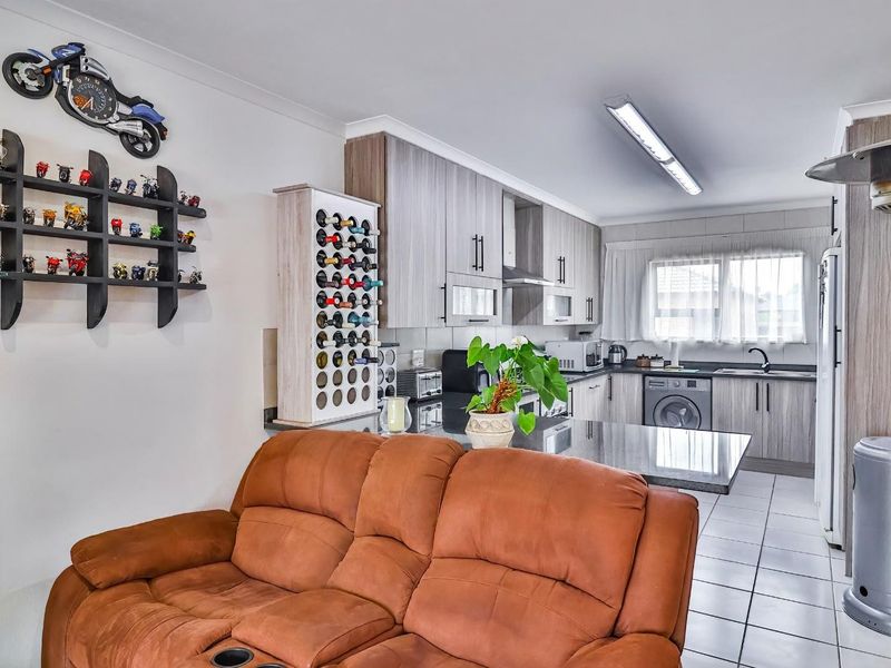 Open-plan kitchen and living area featuring modern wood-grain cabinetry, granite countertops, and tiled flooring, providing a functional and cohesive living space.