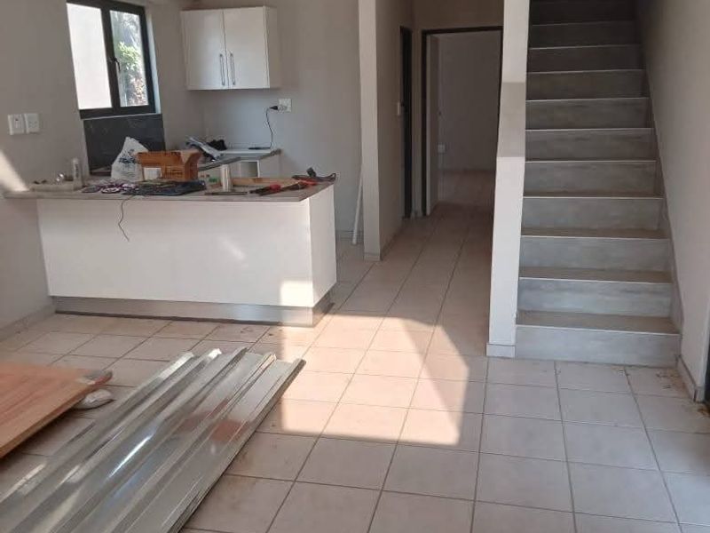 Open-plan living area featuring tiled floors, a kitchen island with cabinetry, and a staircase leading to the upper level.