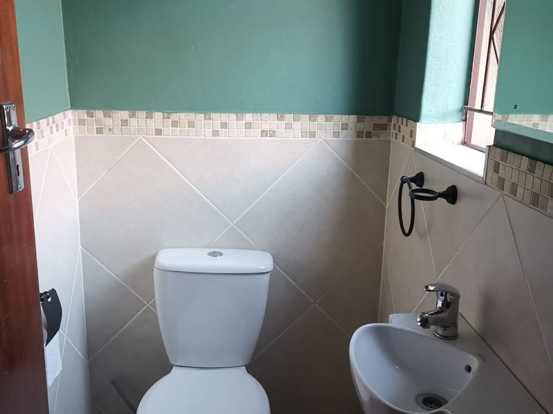 A compact guest bathroom featuring a white toilet, wall-mounted basin with mixer tap, and neutral wall tiling with a decorative mosaic border.
