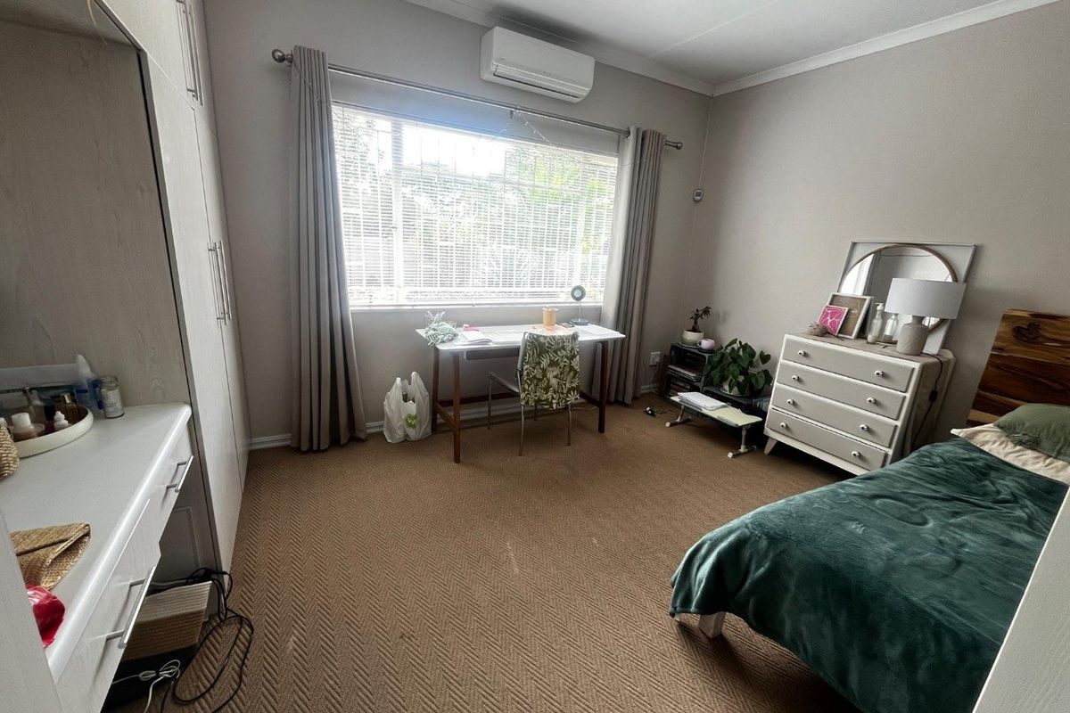 A well-proportioned bedroom featuring built-in cupboards, wall-mounted air conditioning unit, and large window providing natural light.