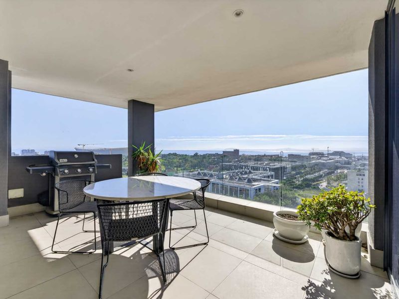 Spacious covered balcony featuring a glass balustrade and expansive panoramic city and ocean views, perfect for outdoor entertaining.