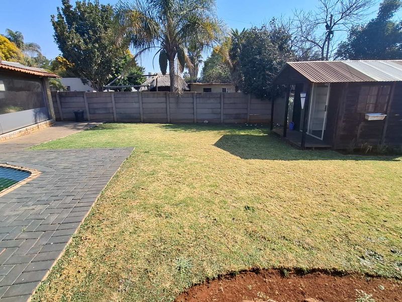 A spacious rear garden featuring a paved patio area, a swimming pool, and a detached timber shed with a corrugated metal roof.