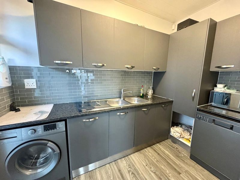 Modern kitchen featuring grey cabinetry, subway tile backsplash, granite countertops, and a double stainless steel sink with integrated laundry space.