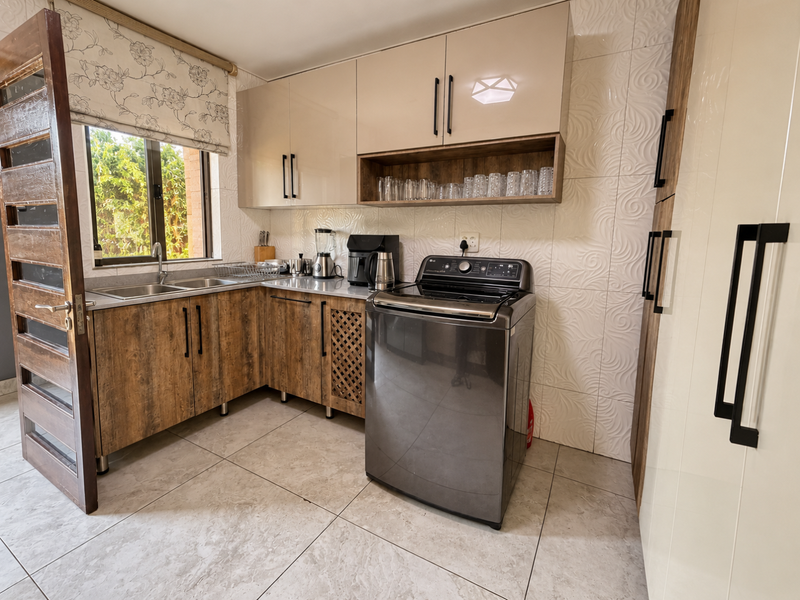 A well-appointed laundry room featuring modern wood-grain and high-gloss cabinetry, stainless steel sink, and durable tiled finishes.