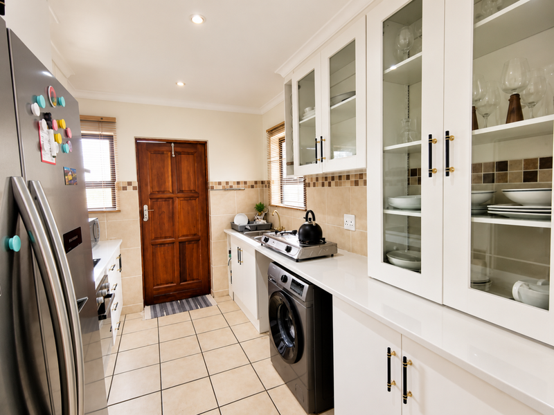 A well-maintained kitchen featuring white cabinetry, quartz countertops, a tiled backsplash, integrated washing machine, and gas hob with glass-fronted display storage.