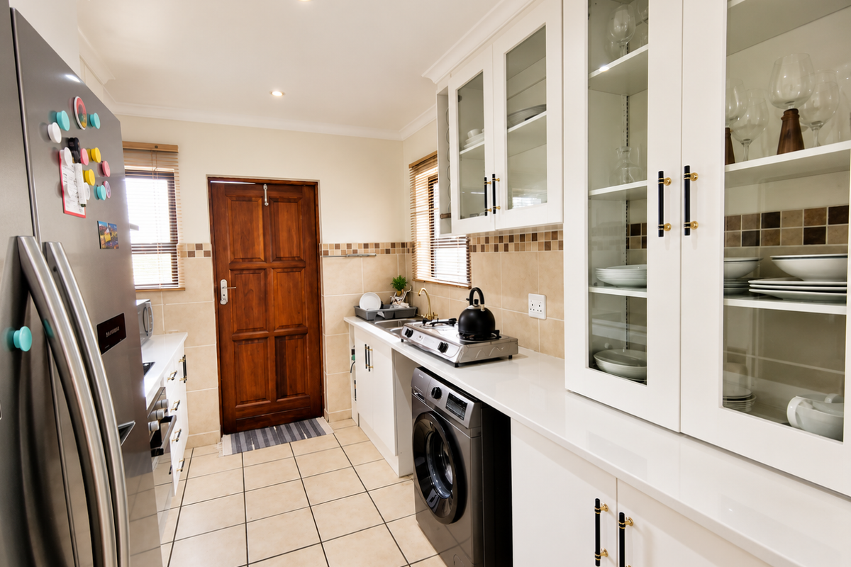 A well-maintained kitchen featuring white cabinetry, quartz countertops, a tiled backsplash, integrated washing machine, and gas hob with glass-fronted display storage.