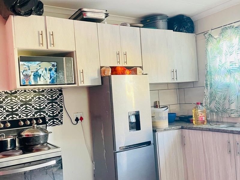 A functional kitchen featuring light wood-grain cabinetry, tiled backsplash, stainless steel sink, and built-in microwave space.