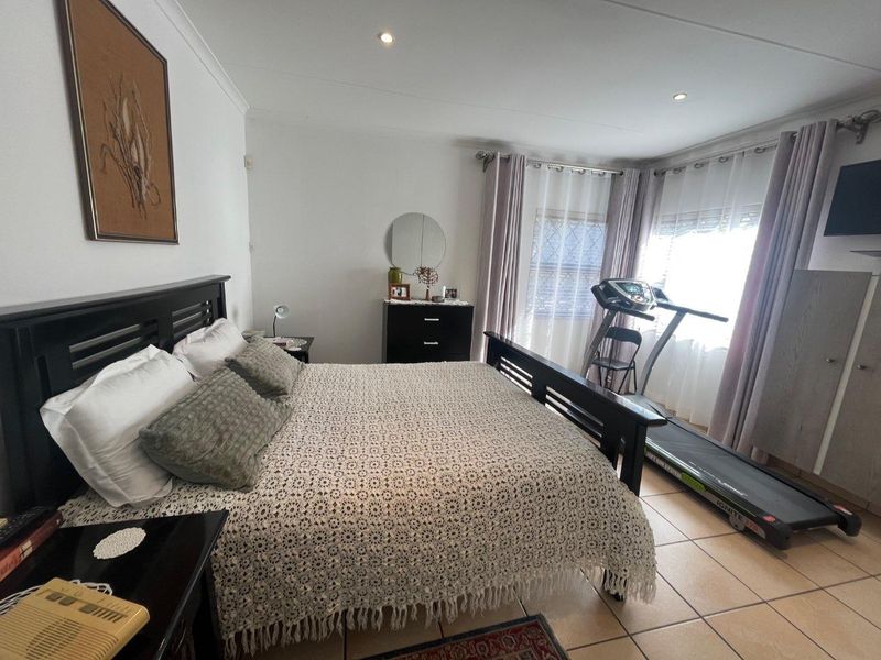 A spacious bedroom featuring neutral tiled flooring, recessed downlighting, and large windows with installed curtain rails.