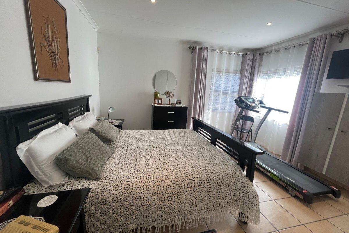 A spacious bedroom featuring neutral tiled flooring, recessed downlighting, and large windows with installed curtain rails.