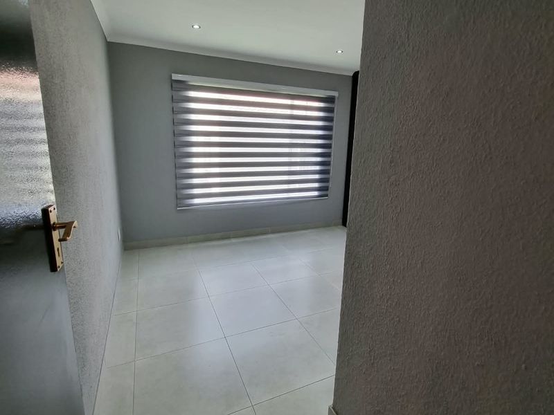 A clean, empty bedroom featuring neutral tiled flooring, recessed downlighting, and modern roller blinds, offering a blank canvas for personalization.