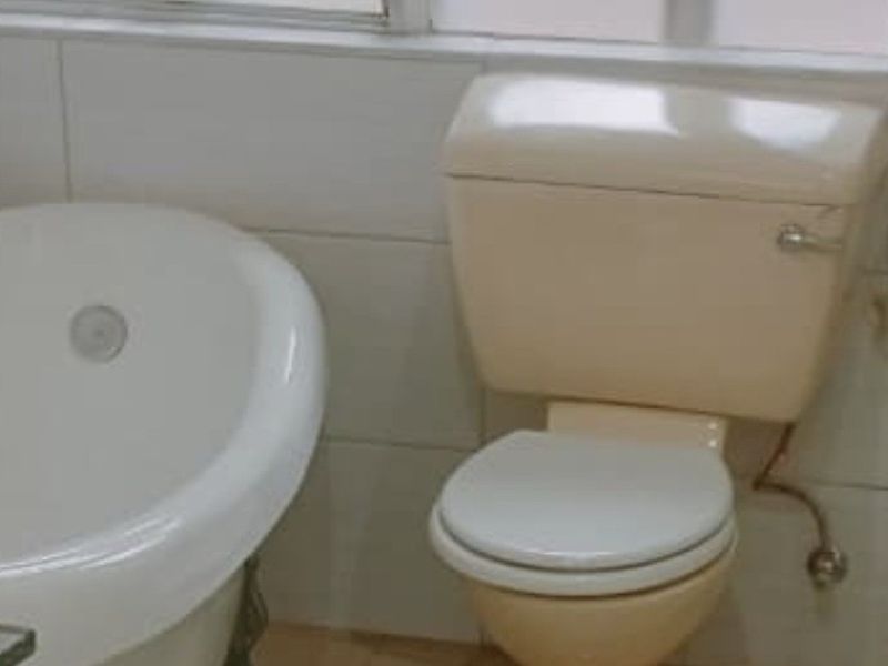 A dated bathroom featuring a white clawfoot bathtub and a cream-colored toilet with tiled walls and flooring.
