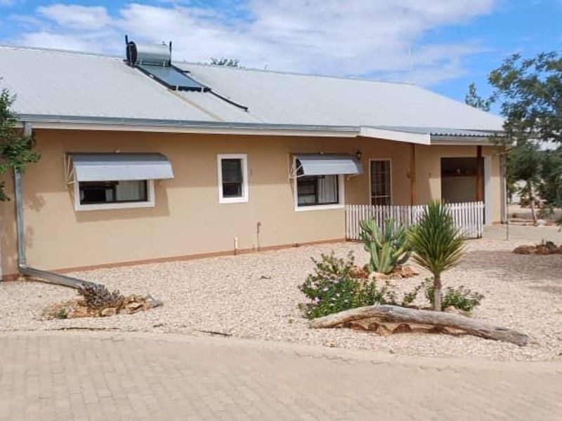 A well-maintained single-story home featuring a corrugated metal roof with a solar water heater, metal window awnings, and a landscaped gravel garden.