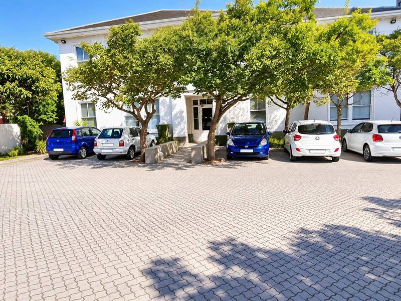 Front exterior view of the office building featuring a paved parking area, mature trees, and a secure gated entrance.