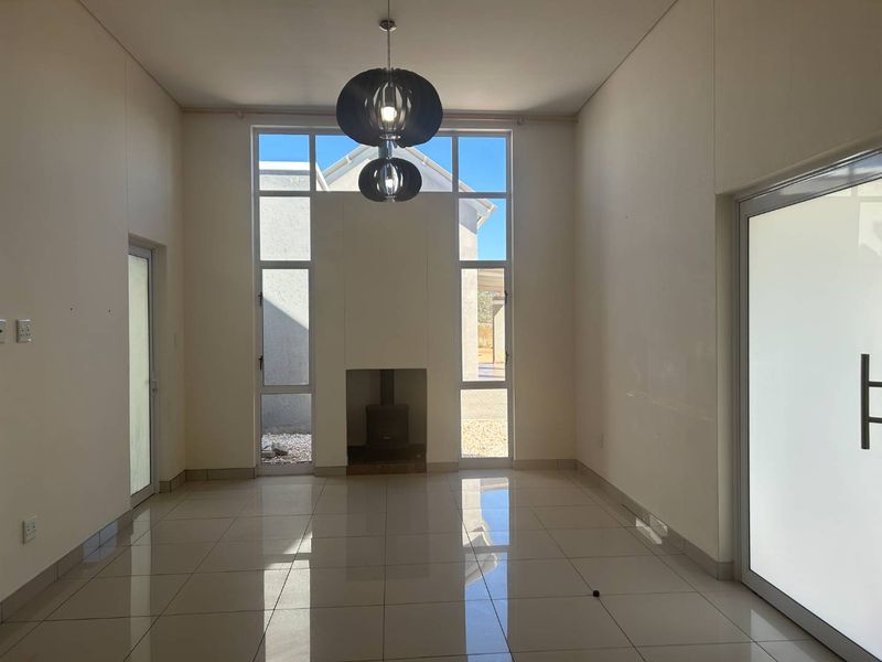 Spacious living area featuring high ceilings, large windows, tiled flooring, and a built-in fireplace, offering a bright and open atmosphere.