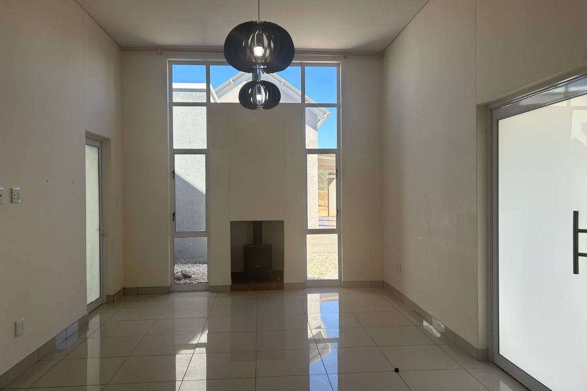 Spacious living area featuring high ceilings, large windows, tiled flooring, and a built-in fireplace, offering a bright and open atmosphere.