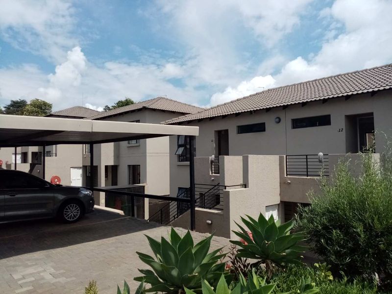 Exterior view of a modern apartment complex featuring a paved driveway, covered carport, and multi-level residential units with tiled roofing.