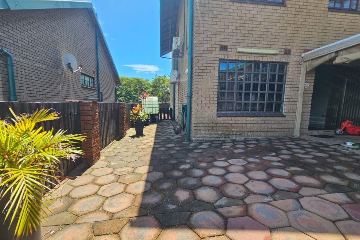 A rear exterior view of the apartment featuring a paved patio area, brick facade, and perimeter timber fencing.