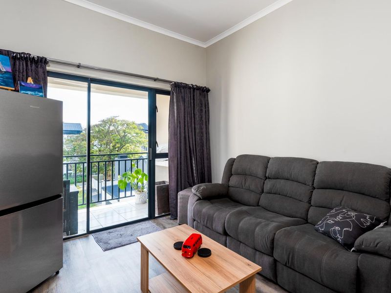 A bright living room featuring laminate flooring and a sliding glass door that opens onto a private balcony with neighborhood views.