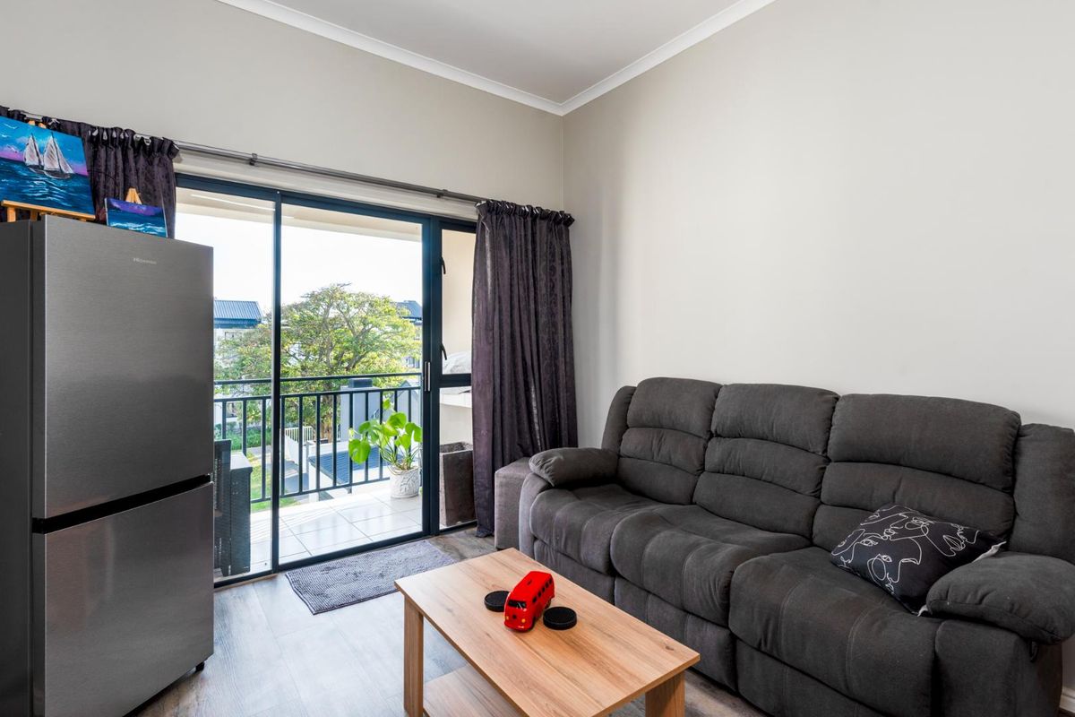 A bright living room featuring laminate flooring and a sliding glass door that opens onto a private balcony with neighborhood views.