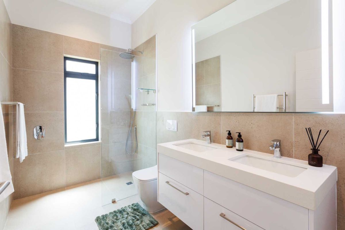 Modern bathroom featuring a double vanity with integrated lighting, a spacious walk-in shower with glass screen, and neutral floor-to-ceiling tiling.