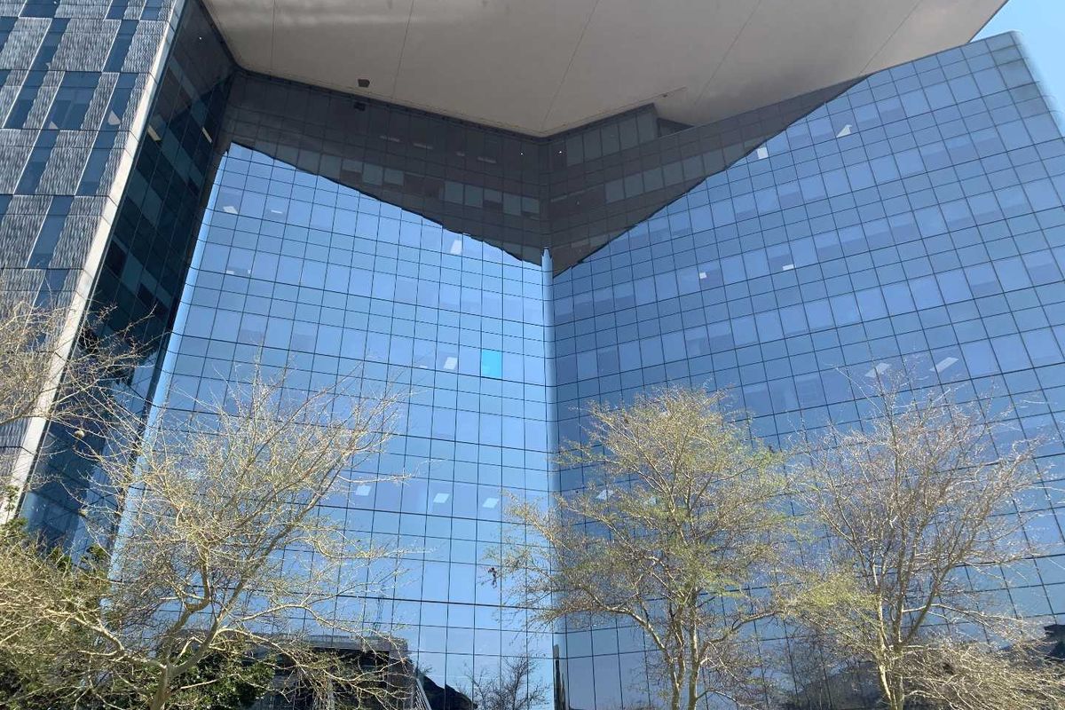 Modern commercial office building featuring a striking glass curtain wall facade and a prominent overhanging roof structure.