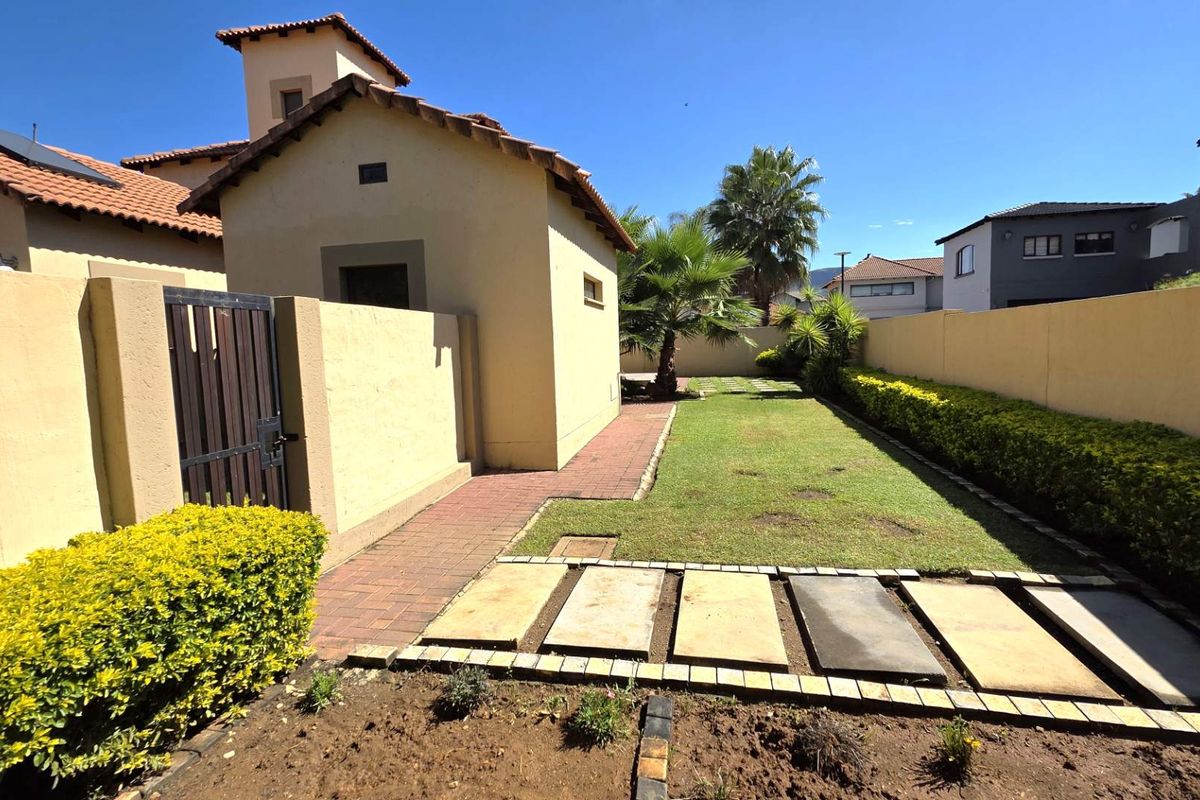 A private rear garden featuring a paved walkway, manicured lawn, perimeter boundary walls, and established landscaping.