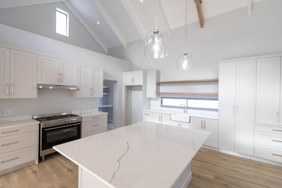 Modern kitchen featuring a large central island, white cabinetry, stone countertops, farmhouse sink, and high vaulted ceilings with exposed timber beams.