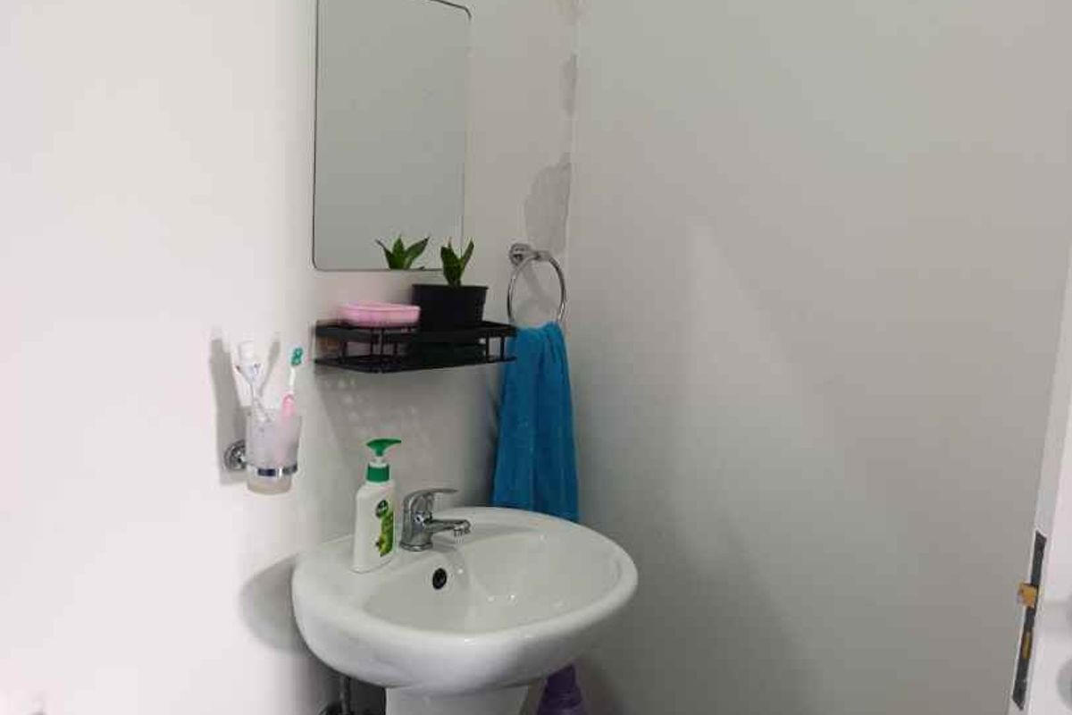 A compact bathroom featuring a white pedestal basin with chrome fixtures and visible wall damage requiring maintenance.